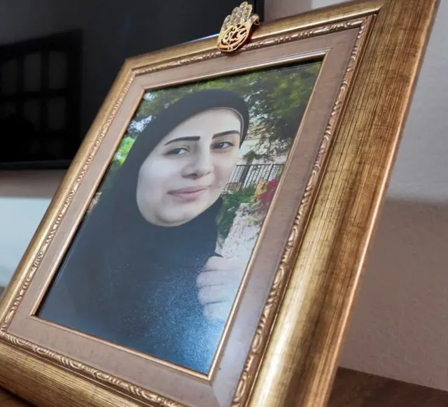 Rafta Nayfe'nin çerçeveli bir fotoğrafı var, kameraya doğru bakıyor.