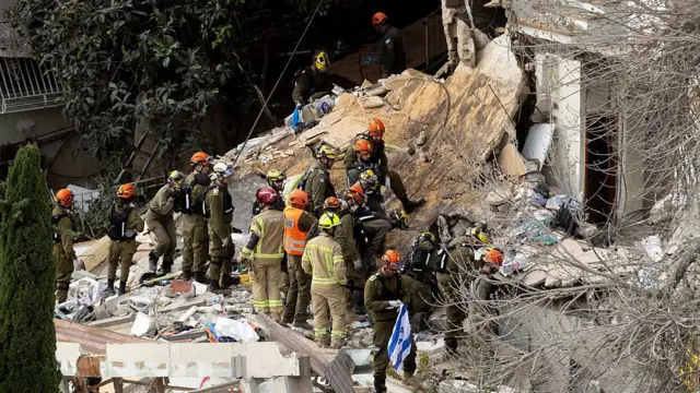 İsrail'de acil durum ekipleri, 6 Nisan 2026'da Hayfa'da İran'ın balistik füze saldırısı sonucu hasar gören bir binadan konut binasından cesetleri çıkarmaya çalışıyor. 
