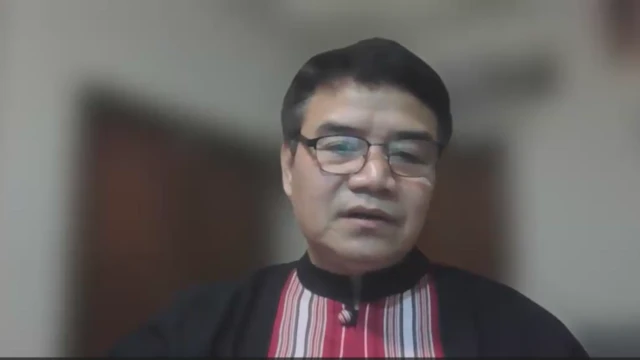 အနက်ရောင်နဲ့ အနီရောင်အစင်းကြားတွဲစပ်ထားတဲ့ကရင်နီအမျိုးသားအင်္ကျီ ဝတ်ဆင်ကာ မျက်မှန်တပ်ထားတဲ့ ဒုတိယဝန်ကြီး ခူးဒယ်နီရယ် 