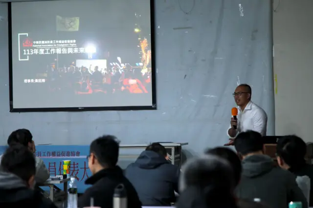 黄钰翔担任消防员工作权益促进会理事长，在会员大会上报告工作进度。