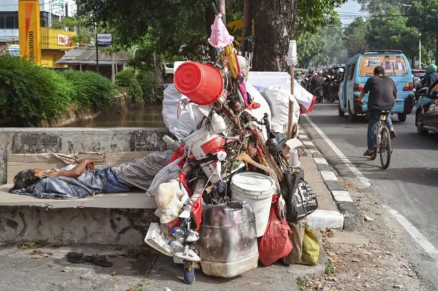 Seorang tunawisma (kiri) tidur di jalan dekat gerobaknya pada jam sibuk pagi hari di Jakarta pada 5 November 2024. 