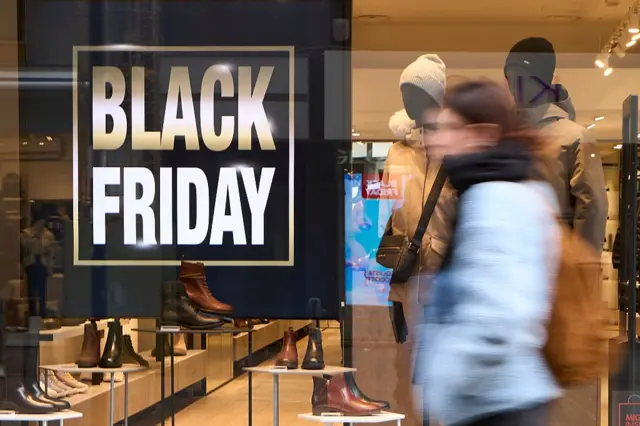 Mulher passa em frente a vitrine com uma placa de Black Friday