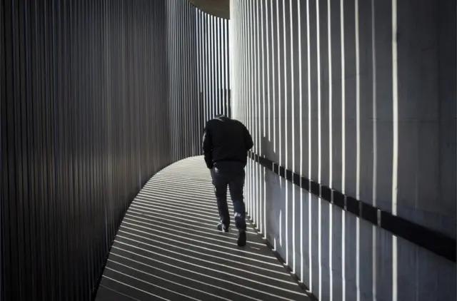 A man walks through shafts of light and shadow.