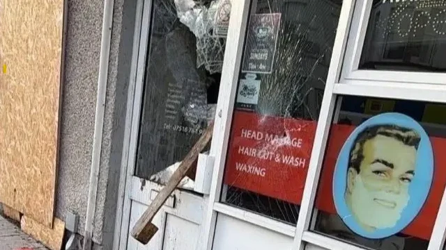 Jendela toko tukang cukur hancur. Beberapa boarding telah dipasang di sebelah jendela. Kayu tergantung di luar pintu.