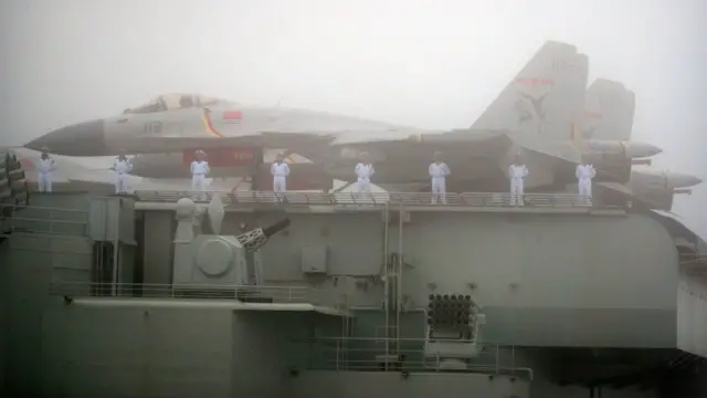 Des marins se tiennent près d'avions de chasse sur le pont du porte-avions Liaoning de la marine de l'Armée populaire de libération (APL) chinoise, alors qu'il participe à une parade navale pour commémorer le 70e anniversaire de la fondation de la marine de l'APL chinoise, en mer, près de Qingdao, dans le Shandong, dans l'est de la Chine.