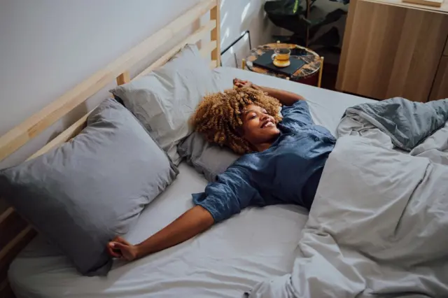 A woman smiles as she sleeps alone in a bed