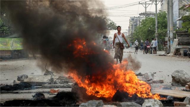 A demonstrator looks on along burning debris during a protest against the military coup in Mandalay, Myanmar, 21 March 2021.