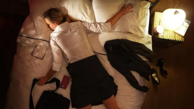 Una mujer tirada en su camina, con la ropa de trabajo y la cartera