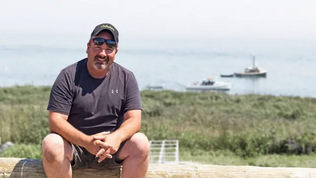 Anthony Ross, sentado, con una bahía con barcos de fondo. 