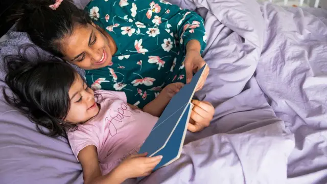 yatakta çocuğuna kitap okuyan bir kadın