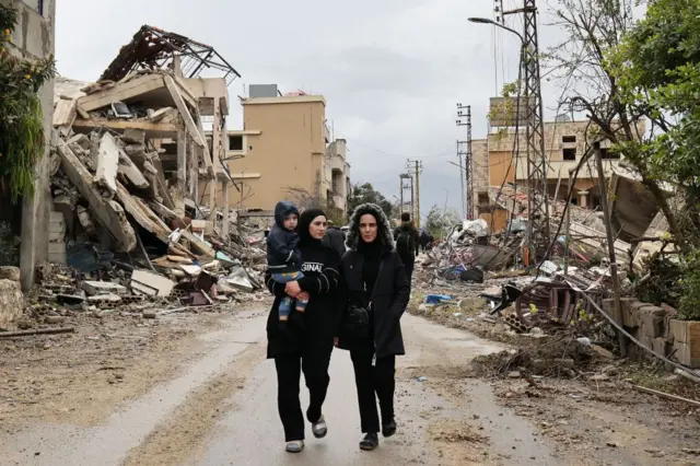 دو زن و کودکی در آغوش از میان ویرانه‌ها عبور می‌کنند