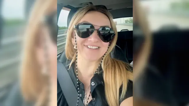 بولينا أزارنيخ تنظر مباشرة إلى الكاميرا وهي جالسة في سيارة. لديها شعر أشقر طويل وترتدي نظارة شمسية كبيرة وقميصًا أسود وتبتسم.