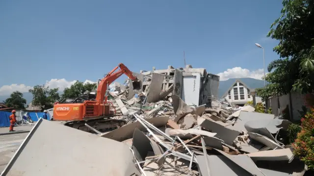 Excavator menyingkirkan puing-puing bangunan hotel.