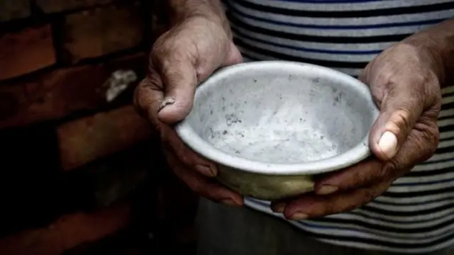 Mãos de um homem segura tigela de metal vazia, sem comida