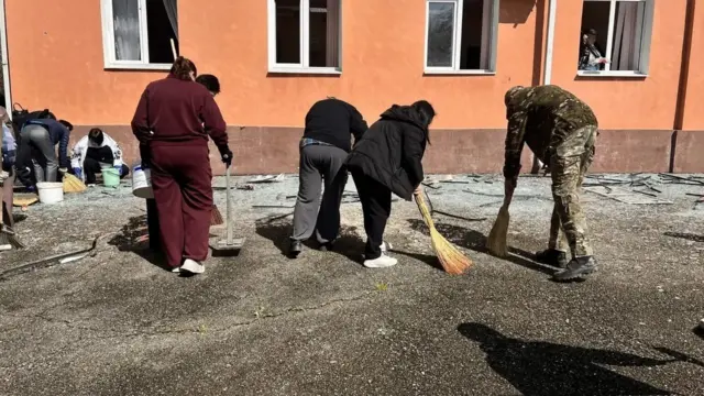 Люди подметают выбитое стекло у здания