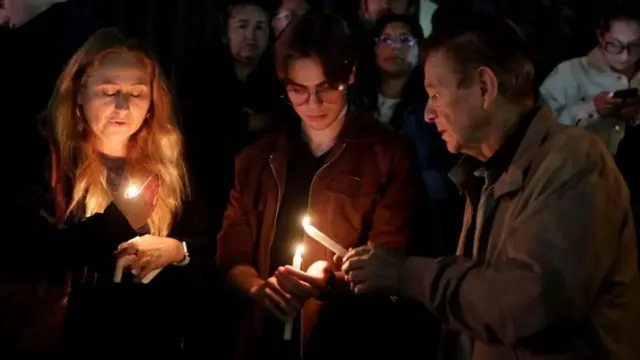 人々がろうそくを手にして屋外にたたずんでいる