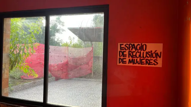 Une autre image prise depuis l'intérieur du site commémoratif. Il montre une grande fenêtre avec une pancarte à côté, accrochée à un mur rouge vif, sur laquelle on peut lire « Centre de détention pour femmes ». 