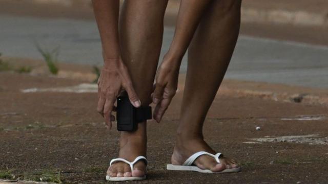 Pessoa com mãos próximas a tornozeleira eletrônica presa em sua perna direita