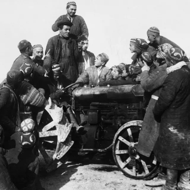 Siyah beyaz fotoğrafta Özbek çiftçiler bir traktör benzeri araca tırmanmış.