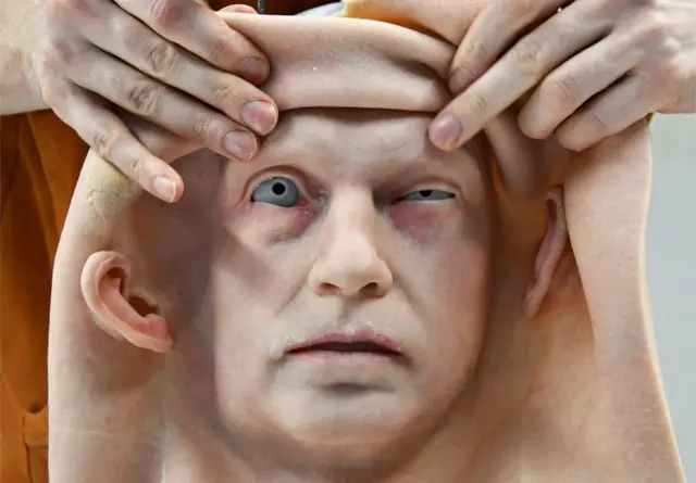 A person fits artificial skin on to the head of a robot