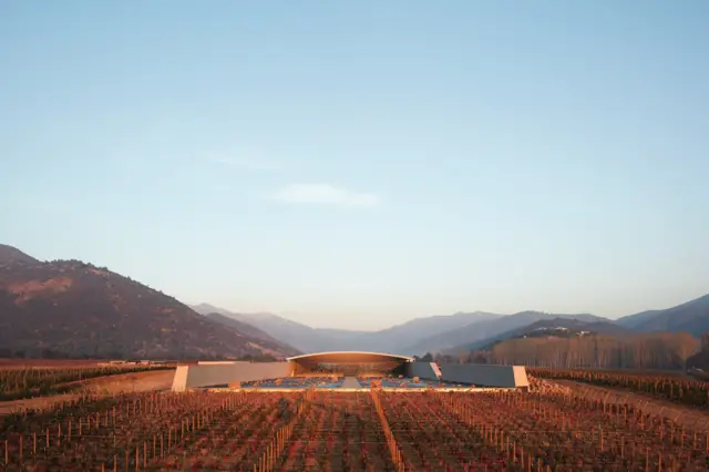 Bodega de arquitectura moderna integrada en un valle con viñedos y montañas al amanecer.