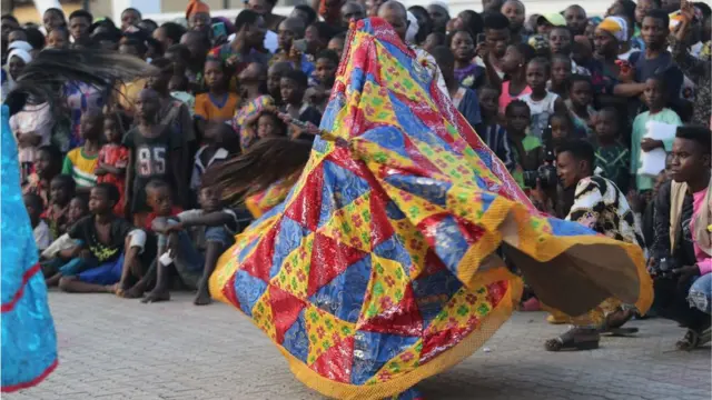 Mutum sanye da kayan dodanni, kayan na reto a jikinsa ya yin da yara ke zaune su na kallo.