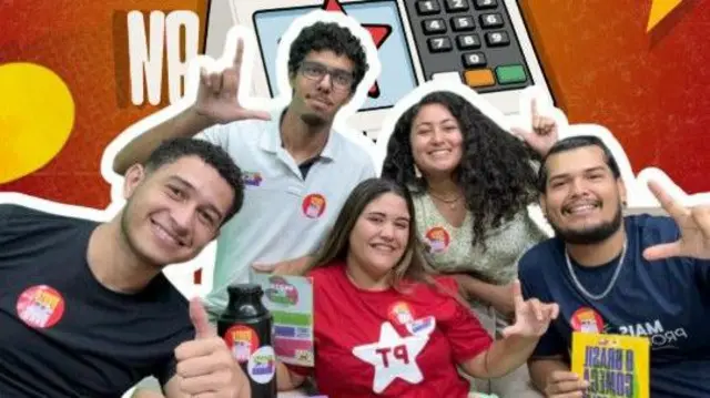 Grupo de jovens com camisa do PT e adesivos. Atrás deles há um desenho de urna. Eles fazem o sinal de L com as mãos