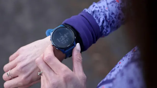 Um close de uma mulher consultando seu smartwatch, pressionando botões e observando as estatísticas que aparecem na tela