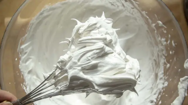 Рука с венчиком и взбитые белки