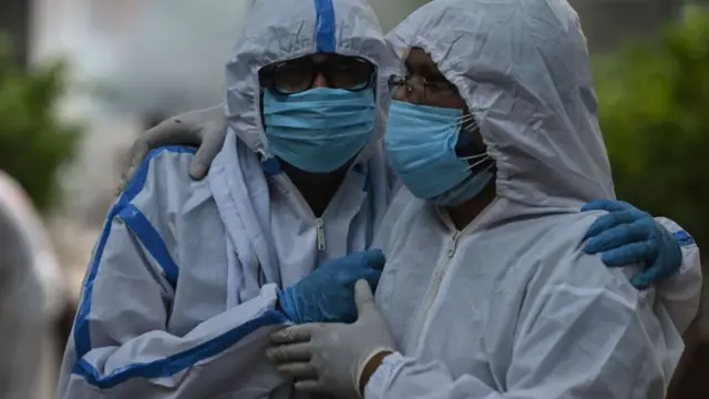Personas con trajes de protección se abrazan.