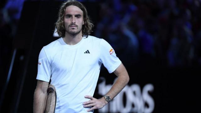 Stefanos Tsitsipas stands with his hands on his hips, his trophy tucked under his right arm