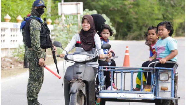 An armed security personnel wearing a face mask guards a road check point in Nong Chik district to screen motorists and people returning from Malaysia in Thailand"s southern province of Pattani on March 24, 2020