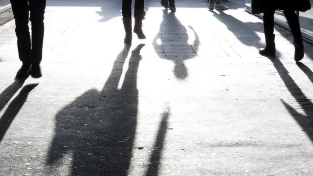 أشخاص يسيرون في الشارع ويبدو ظلهم واضحا أمامهم