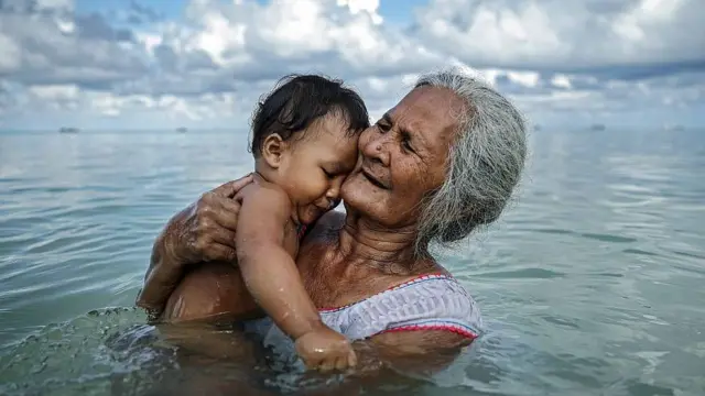 À Tuvalu, une grand-mère baigne son petit-fils dans un lagon intérieur.