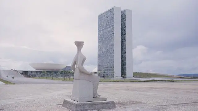 Estátua que fica na frente do STF com Congresso Nacional ao fundo