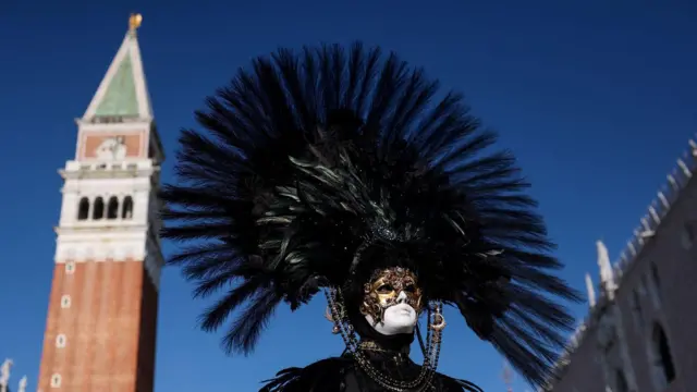 Čovek na licu ima paunovo perje iza se vidi toranj crkve Svetog Marka u Italiji