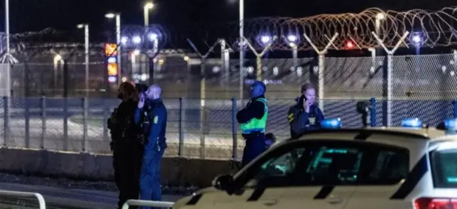 Поліцейські стоять біля паркану аеропорту біля поліцейської машини і дивляться в небо 