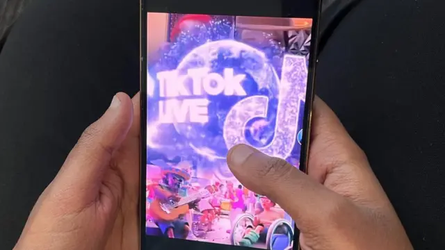 Une photo montrant les mains d'une personne tenant un téléphone portable avec TikTok Live à l'écran.