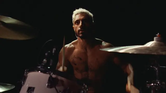 Riz Ahmed interpretando baterista, tocando instrumento