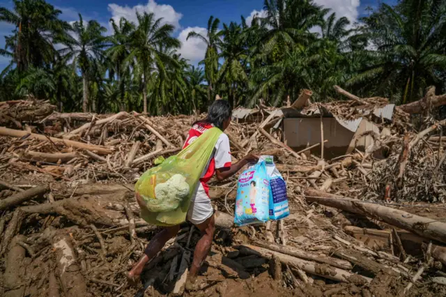 Warga melintasi jalan akses antardesa pascabanjir bandang di Desa Tanjung Karang, Karang Baru, Kabupaten Aceh Tamiang, Aceh, Minggu (7/12/2025). Akses penghubung Desa Tanjung Karang dan Desa Menang Gini yang sempat tertutup tumpukan kayu gelondongan akhirnya bisa terbuka usai pemerintah mengerahkan alat berat untuk pembersihan sehingga mobilitas masyarakat, termasuk distribusi bantuan menjadi bisa dilakukan. 