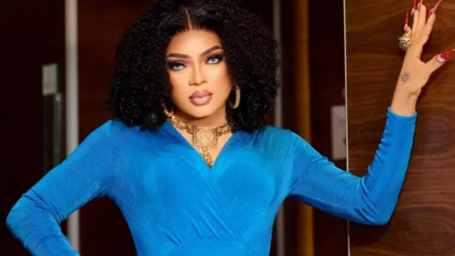 Bobrisky dressed in blue outfit wit earrings and neck chains