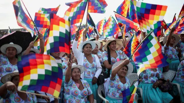 
Mulheres levantam bandeiras indígenas em um encontro político.
