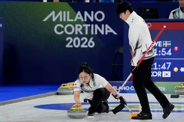 컬링 믹스더블 정영석과 김선영. 김선영이 컬링 스톤을 얼음 위로 신중하게 굴리고 있고, 뒤에서는 브러시를 든 정영석이 스위핑을 준비하고 있다.