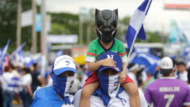 Dos adultos y un niño enmascarados con la bandera de Nicaragua.
