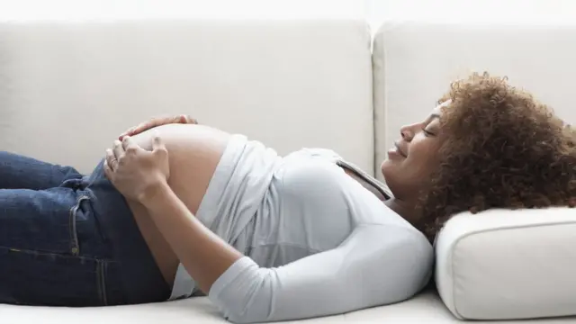 Una mujer embarazada acostada en un sofá se toca su barriga