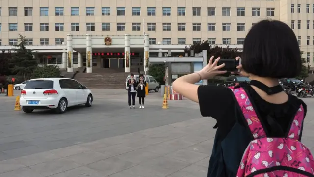 游客在河北雄县政府办公大楼前留影。