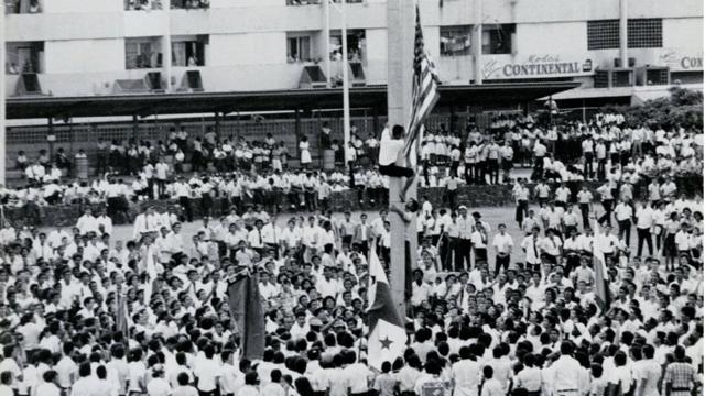 Protesta en la frontera entre Panamá y la Zona del Canal, en la que un joven sustituye la bandera estadounidense por la panameña.