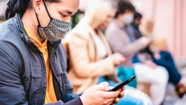 Personas con mascarilla mirando el teléfono.
