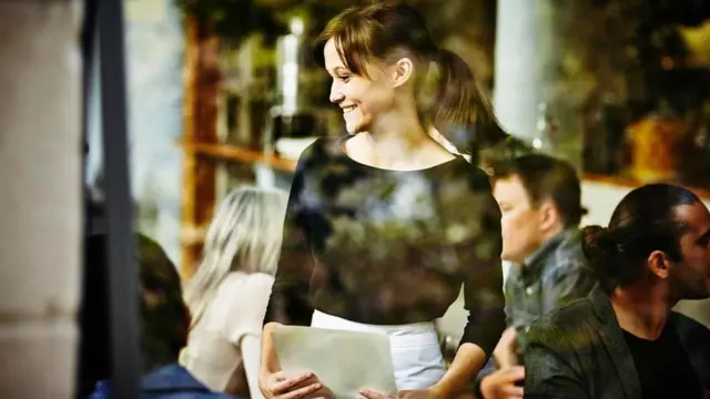 عملاء في مطعم ونادلة تبتسم لهم