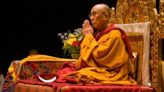 O 14º Dalai Lama, sentado com as mãos postas